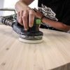 Super-Seat | Page Title | A person is sanding a round, light oak table with a black and green sander. |. | Hospitality Furniture