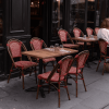 Super-Seat | Was Sie brauchen, sind Stühle, Tafeln, Barkassen, Picknick-Tafeln und andere Tafeln und Stühle. | Rode metalen Café de Paris stoelen en tafels met glazen staan buiten bij een donkere gevel; iemand zit alleen. | Horecameubilair
