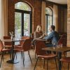 Super-Seat |A woman and a man sit at a restaurant table.... Black vintage leather chairs & red chairs at tables, brick wall, large windows. | Hospitality Furniture