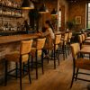 Super-Seat | Eine Frau sitzt allein an einer Bar... | Barkrukken in okergeel velours met zwart metalen poten, houten vloer en bakstenen muren. | Horecameubilair