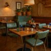 Super-Seat | A cozy restaurant interior with vintage green Aviator restaurant chairs featuring gold frames, wooden tables set with glasses and candles, potted plants, wall art, and warm lighting from woven pendant and wall sconce. | Vintage groene stoelen met gouden metalen frame, houten tafels, glazen, kaarsen en warme rotan verlichting. | Horecameubilair