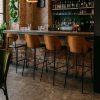 Super-Seat | A bar with a stone floor, brick wall and four New York designer bar stools wood black leather. | Four black leather bar stools with wooden legs; bar with stone floor and interior wall. | Hospitality Furniture