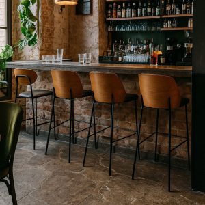 Super-Seat | A bar with a stone floor, brick wall and four New York designer bar stools wood black leather. | Four black leather bar stools with wooden legs; bar with stone floor and interior wall. | Hospitality Furniture