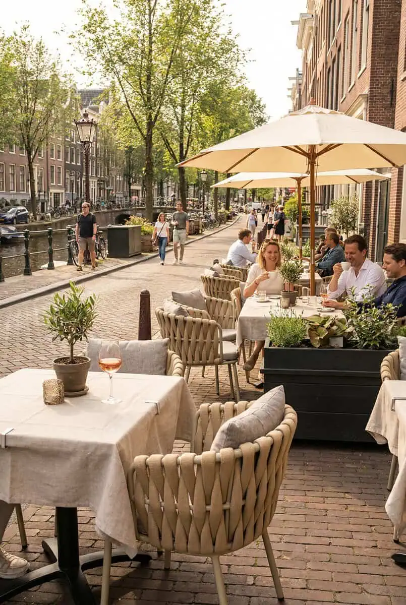 Super-Seat |Taupe metal stacking chairs and tables under taupe umbrellas along a canal surrounded by greenery. | Hospitality Furniture