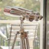 Super-Seat | Silver chrome binoculars on wooden tripod; in background a wooden chair, green outside. | Hospitality Furniture