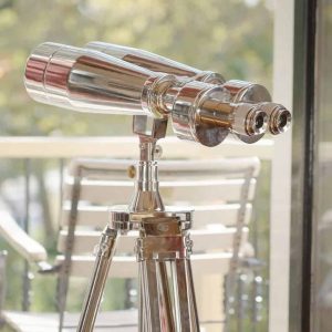 Super-Seat | Silver chrome binoculars on wooden tripod; in background a wooden chair, green outside. | Hospitality Furniture